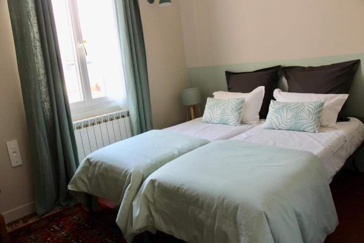 A double bed with two pillows, a bedside lamp, and a window with curtains.