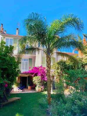 Un edificio residencial con jardín, que incluye una palmera y plantas con flores.