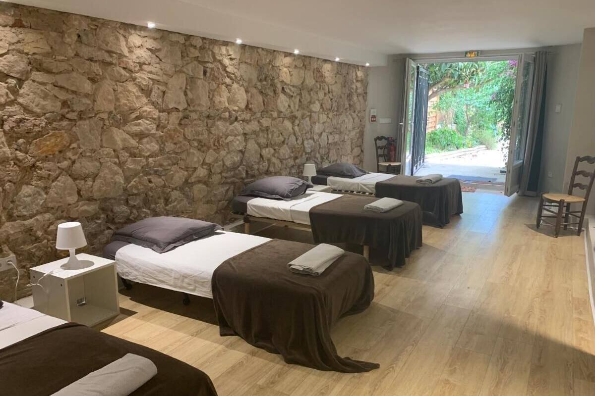 A hotel room with three beds, a stone wall, wooden flooring, and a view of greenery outside.