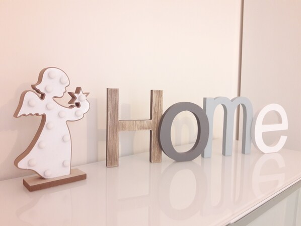 Una figurita decorativa de un ángel y letras de madera que deletrean 'Home' sobre una superficie reflectante.