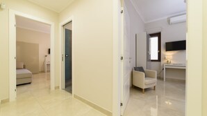 A spacious hallway with a sofa and a chair, a television mounted on the wall, and a door leading to another room.