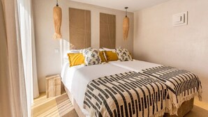 Un letto matrimoniale con una coperta decorata, due lampade a parete e una finestra con tende.