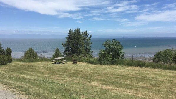 A grassy area with a bench and a picnic table, overlooking a body of water and distant land.
