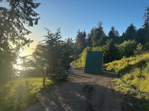 Ein Kiesweg führt zu einem grünen Gebäude, umgeben von Bäumen und wolkenlosem Himmel.
