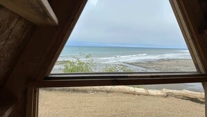 A view from a window with a wooden frame, overlooking a beach with waves and distant horizon. - A-Frame (Site 7) Shelter w/ Incredible Ocean View (Port Angeles)