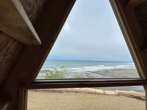 A view from a window with a wooden frame, overlooking a beach with waves and distant horizon. - A-Frame (Site 7) Shelter w/ Incredible Ocean View (Port Angeles)