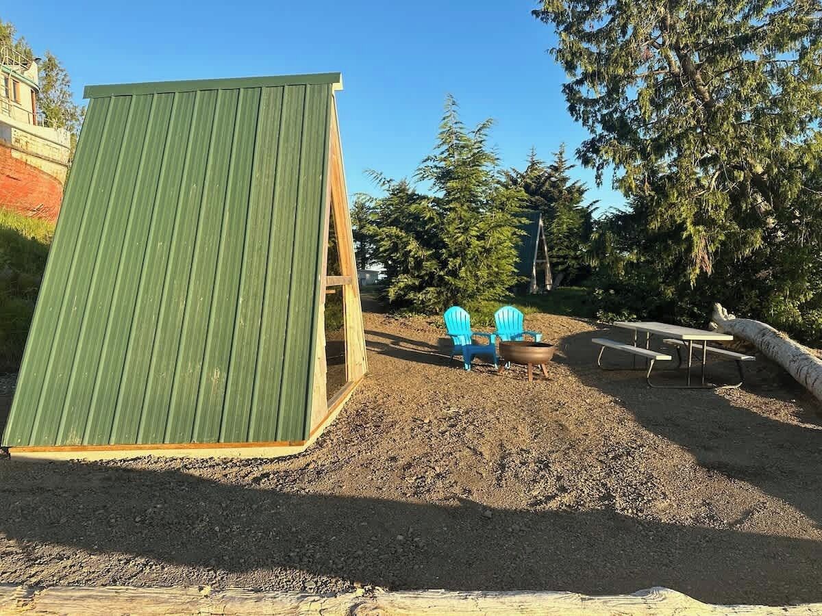 Un espace extérieur abrité, doté d’une structure en bois, de deux chaises bleues et d’une table de pique-nique.