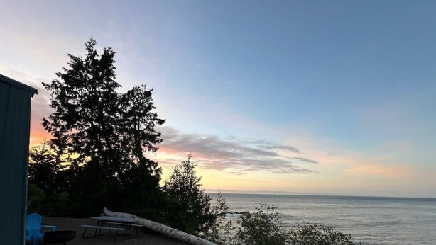 A patio with a table and chairs, overlooking a body of water and a sunset. - A-Frame (Site 7) Shelter w/ Incredible Ocean View (Port Angeles)