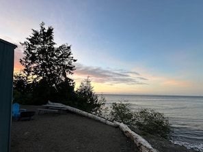 A patio with a table and chairs, overlooking a body of water and a sunset.