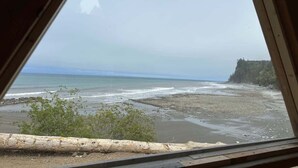 Vista costera a través de una ventana con marco de madera, una playa y un acantilado boscoso.