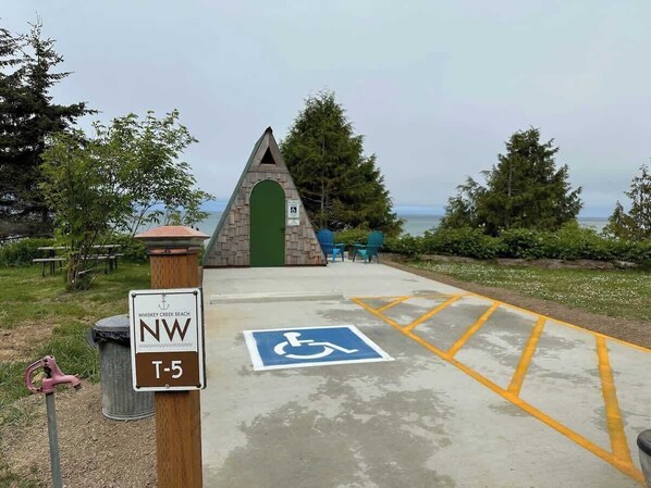 Une aire de stationnement accessible aux personnes en fauteuil roulant, avec un panneau indiquant les places réservées aux personnes handicapées, un panneau de signalisation indiquant la direction de la plage de Whiskey Creek et un marqueur de sentier T-5.