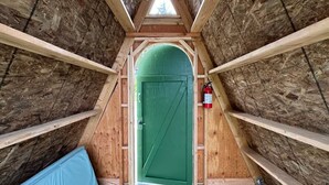 Ein schmales Zimmer im Dachgeschoss mit einer grünen Tür, Holzbalken und einem Feuerlöscher.