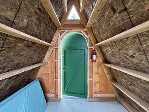 Une petite pièce mansardée avec une porte verte, des poutres en bois et un extincteur.