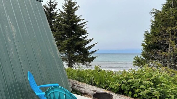 A patio with two blue chairs, a metal trash can, and a view of the ocean.