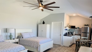 Ein Schlafzimmer mit zwei Betten, einem Deckenventilator, einem Kleiderschrank und einer Küchenzeile mit Kühlschrank und Mikrowelle.