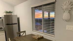 Eine Küche mit einem Holztisch, Stühlen, einem Kühlschrank, einem Fenster mit Jalousien und einer Ananas-Dekoration an der Wand.