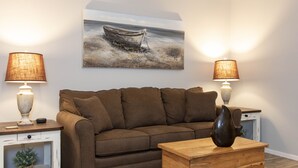 Ein Wohnzimmer mit einem braunen Sofa, zwei Beistelltischen mit Lampen, einem Holztisch und einem Bild eines Bootes an der Wand.