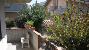 Un balcon avec une chaise en plastique blanche, un pot de fleurs et une rambarde en métal.