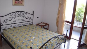 Une chambre à coucher comprenant un lit, une petite table de chevet, un tableau accroché au mur et une porte-fenêtre coulissante donnant sur un balcon.