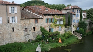 A riverside building with stone walls, a wooden boat, and a person fishing. - Old stone farmhouse in a quiet location with large heated pool. (lavaurette)