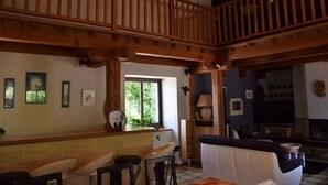 A spacious living area with a wooden balcony, a kitchen with a window, and a seating area with a sofa and bar stools. - Old stone farmhouse in a quiet location with large heated pool. (lavaurette)