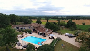 A villa with a swimming pool, surrounded by lush greenery and fields.