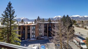 Ein modernes Gebäude mit einer Stein-Fassade, mehreren Balkonen und Blick auf schneebedeckte Berge.