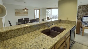 Eine Küche mit Granit-Arbeitsplatten, einer Edelstahl-Spüle, Holzschränken und einem Essbereich mit Stühlen und einem Tisch.