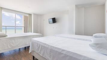 A hotel room with two beds, a TV on the wall, and a window with a view of the sea.