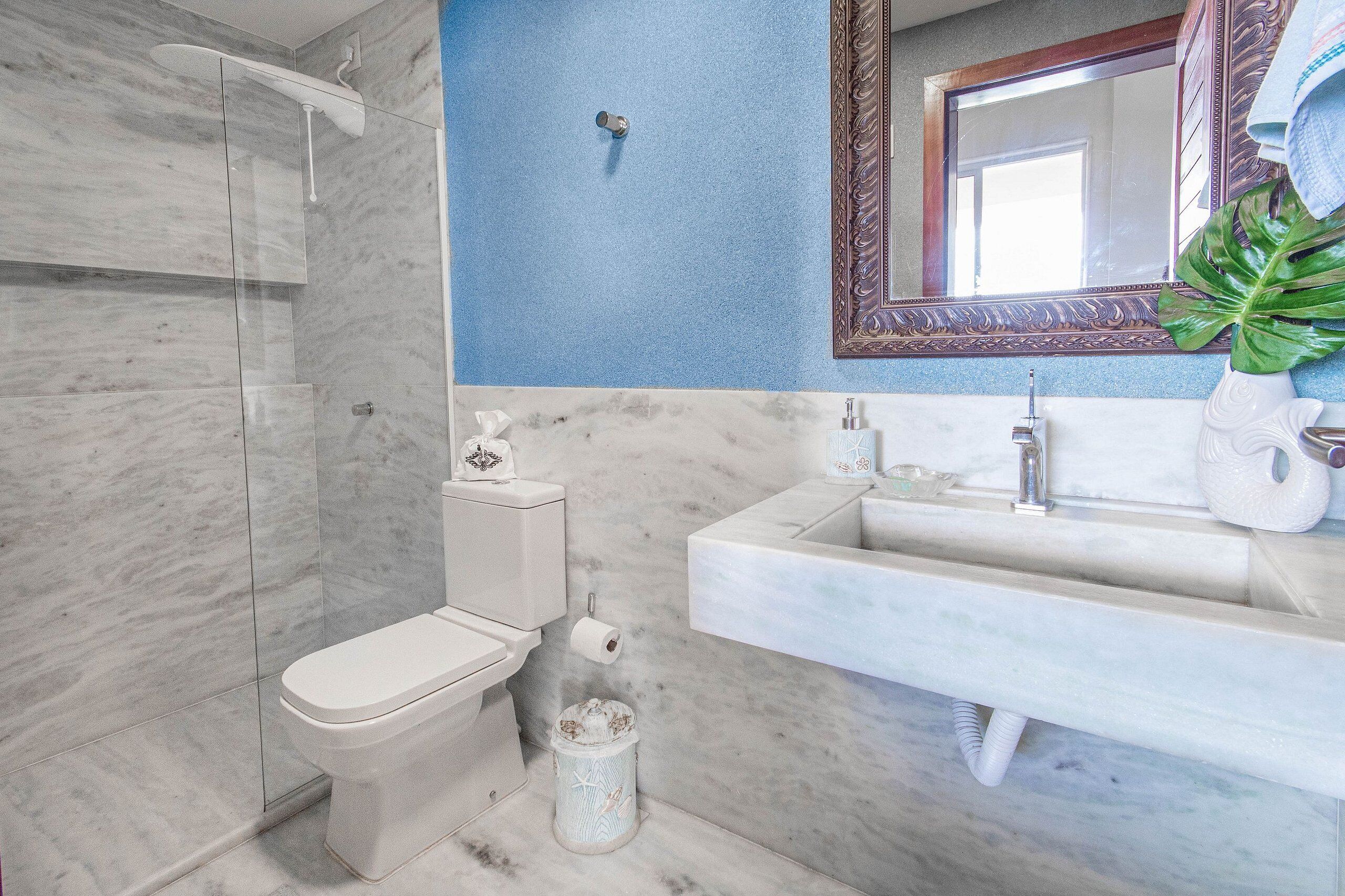 A bathroom with a toilet, shower, sink, and a mirror with a decorative frame.