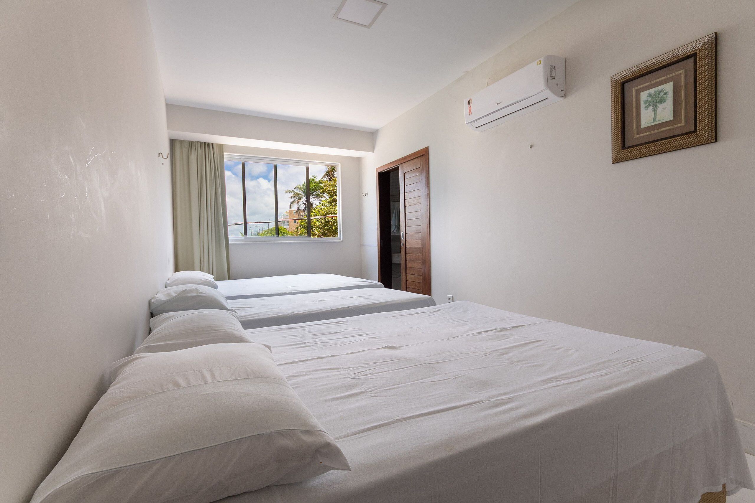 Un dormitorio con dos camas, una ventana con vistas a palmeras y un equipo de aire acondicionado en la pared.