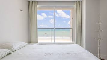 A bedroom with a large bed, a view of the beach, and a window with curtains.