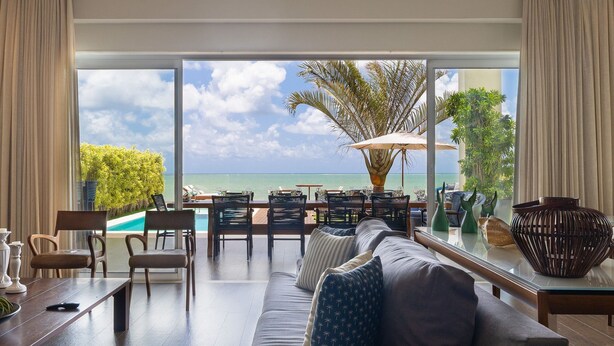 A modern living room with a large glass door leading to a poolside area, featuring a sofa, chairs, and a dining table. - Casa luxuosa a beira mar de Jacumã RN (Ceara-Mirim)