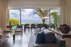 Una sala de estar moderna con un gran ventanal que da a una zona de piscina, que incluye un sofá, sillas y una mesa de comedor.