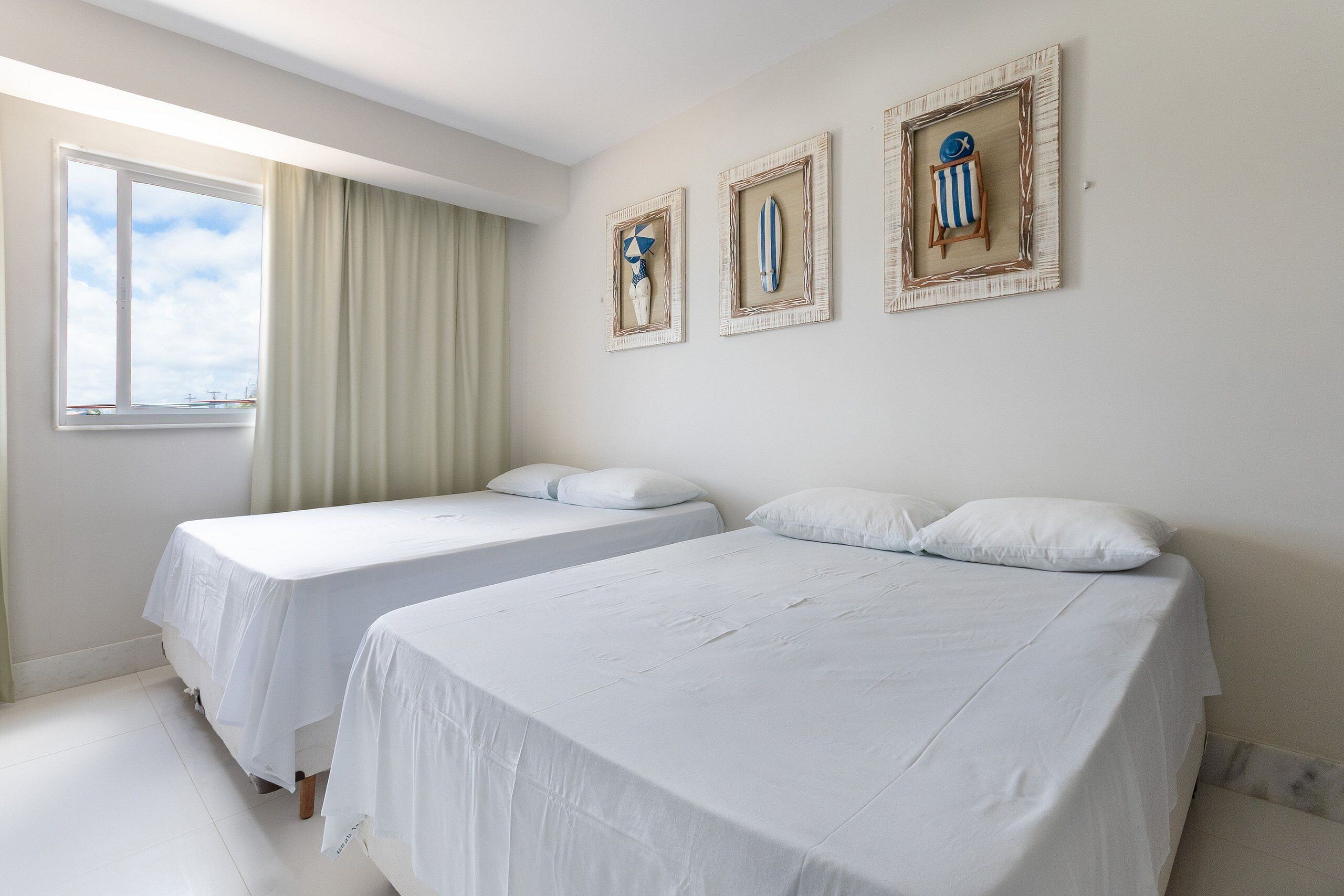 Una habitación con dos camas, una ventana con cortinas y tres cuadros en la pared.