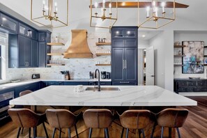 Une cuisine moderne avec des meubles de couleur sombre, un grand îlot central et un luminaire suspendu.