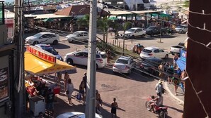 A busy street with parked cars, pedestrians, and a beach in the background. - Pe Na Areia Beach Hostel (Araruama)