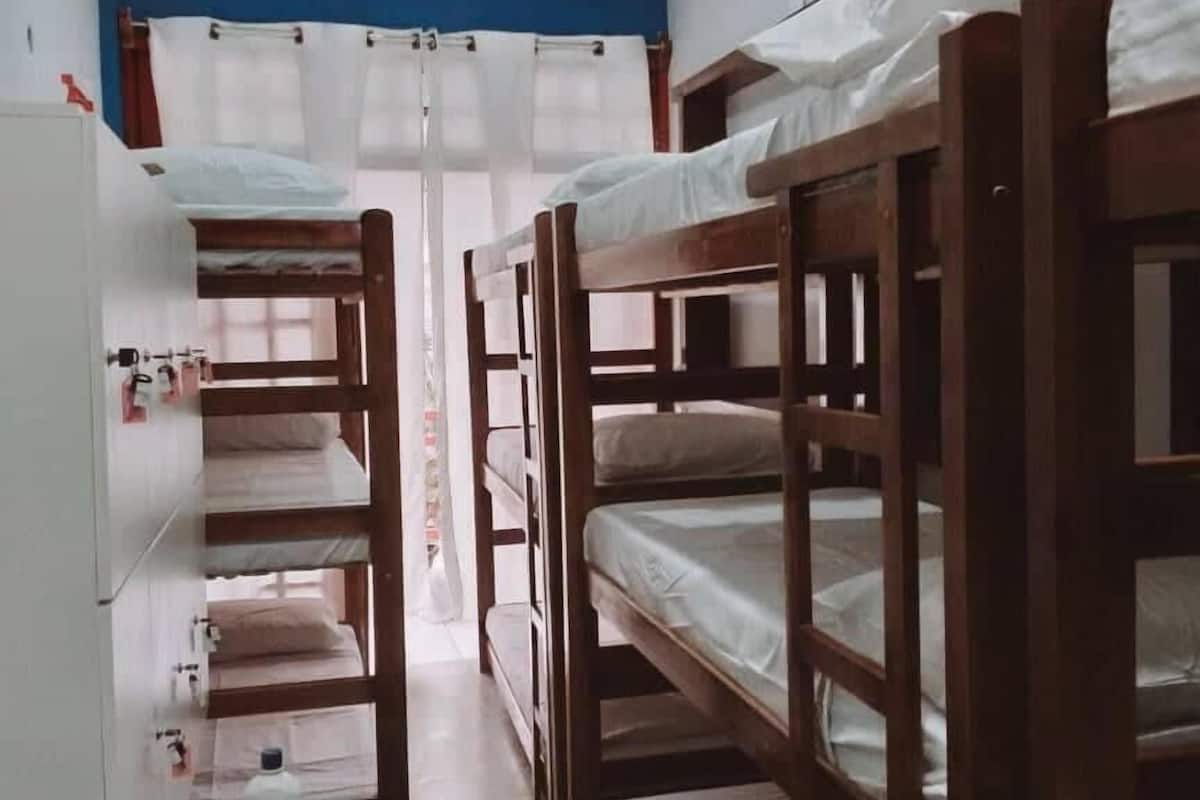 A dormitory room with bunk beds, a white wardrobe, and a small table with a bottle.