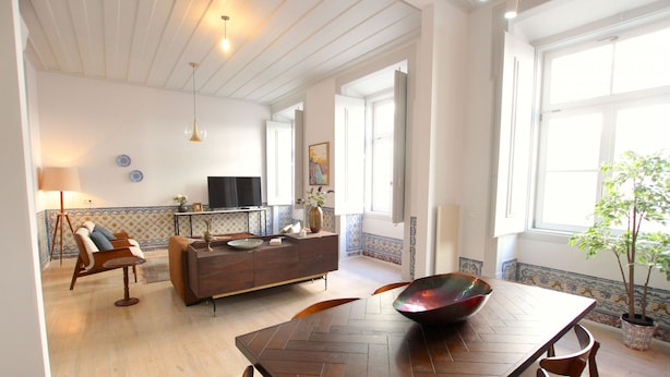 Un vaste espace de vie comprenant une table à manger en bois disposée en motif à chevrons, un canapé et un téléviseur en arrière-plan.