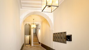 Un couloir doté d’un sol en pierre, d’une porte en arc de cercle, d’un escalier et d’une boîte aux lettres fixée au mur.