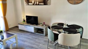 A modern living room with a flat-screen TV, a dining table with black woven placemats, and a wall-mounted clock. - Exclusive pool in apartment area,  5 minutes on foot to beach La Mata (La Mata)
