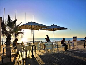 Un café al aire libre con mesas, sillas, sombrillas y vista al océano.
