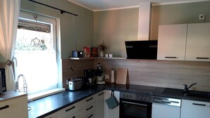 A modern kitchen with white cabinets, a black countertop, and a window with curtains. - Vacation in the southern Harz (Ellrich)