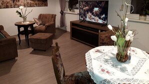 A living room with a television, a sofa, a coffee table, and a decorative vase with flowers. - Vacation in the southern Harz (Ellrich)