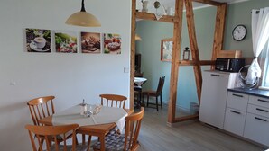 A dining area with a wooden table and chairs, a kitchen with white cabinets, and a clock on the wall. - Vacation in the southern Harz (Ellrich)