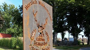 A rustic welcome sign with a deer and text in a foreign language, mounted on a metal post with a grassy area in the background. - Vacation in the southern Harz (Ellrich)