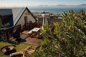 A deck with a table and chairs, overlooking a harbor with boats and a mountainous backdrop. - Sundowner Loft (Mossel Bay)
