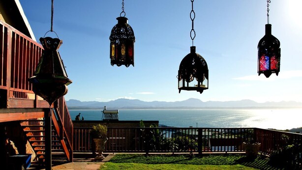 A patio with hanging lanterns, a view of the sea, and a mountain range in the background. - Sundowner Loft (Mossel Bay)