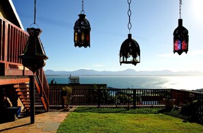 Un patio con faroles colgantes, vista al mar y una cadena montañosa al fondo.