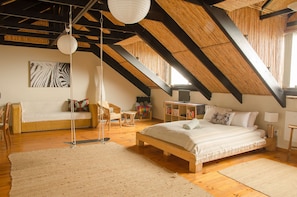 A spacious attic bedroom with a high ceiling, exposed wooden beams, a large bed, a sofa, and a bookshelf.